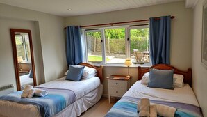 Een slaapkamer met twee bedden, een raam met gordijnen, een nachtkastje en een spiegel.