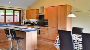 Una cocina moderna con armarios de madera, una isla central con taburetes de bar, una mesa de comedor con mantel estampado de lunares y una lámpara colgante.