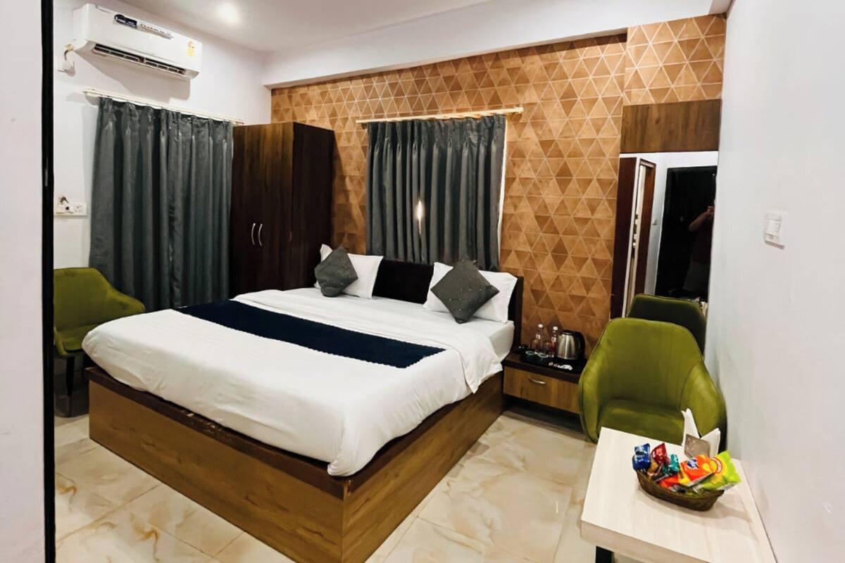 Habitació d'hotel moderna amb un llit gran, un ventilador de sostre, un aparell d'aire condicionat, una taula petita amb aperitius i cadires verdes.