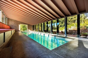 A modern indoor swimming pool with a wooden ceiling and large windows.
