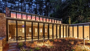 A modern building with large glass windows, a stone pathway, and a forested backdrop. - Historic Retreat in Peak District by River Dane (Wildboarclough)