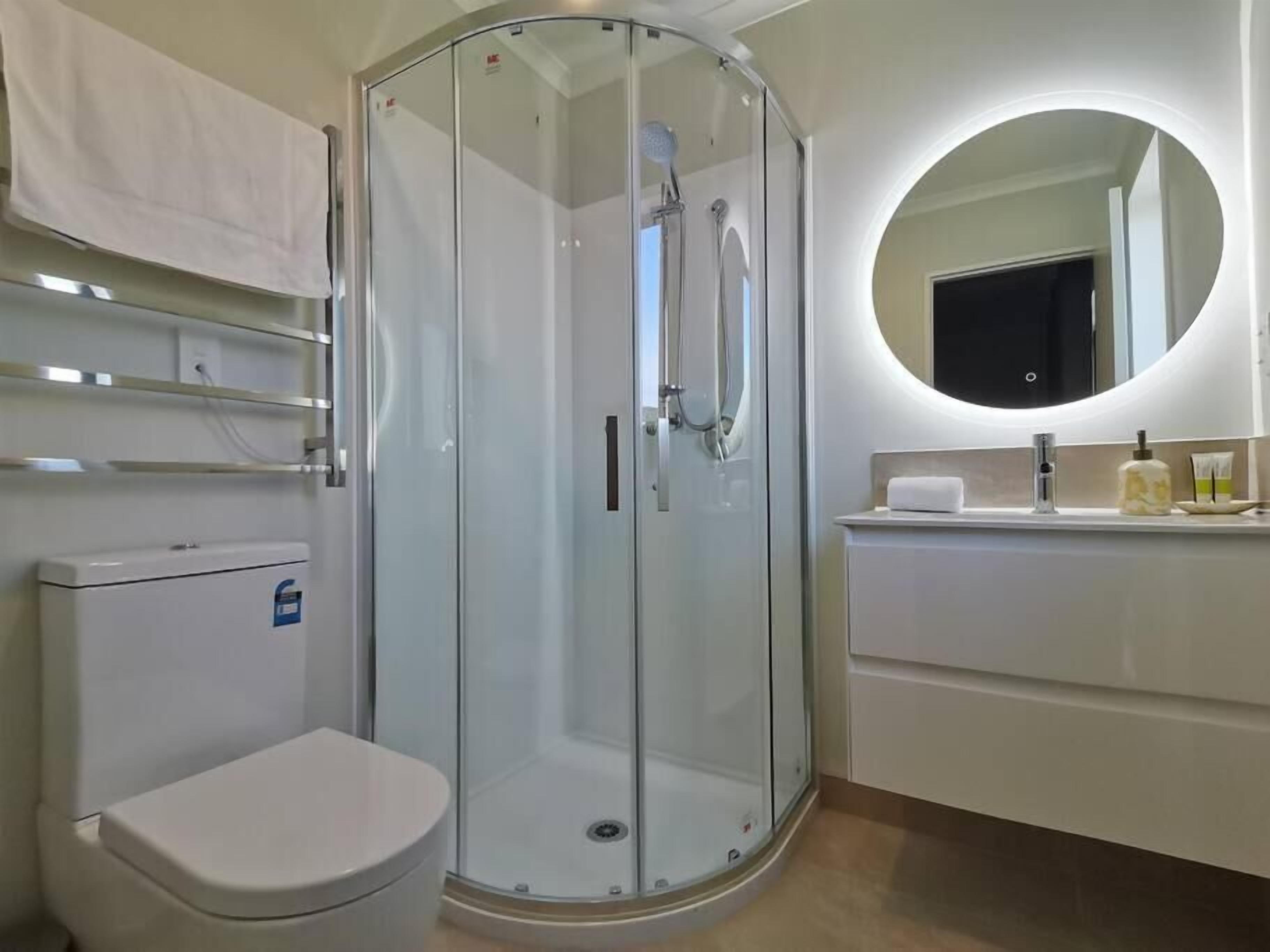 A modern bathroom with a glass-enclosed shower, a toilet, and a vanity with a mirror.