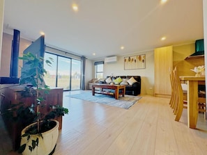 Ein geräumiges Wohnzimmer mit großem Fenster, einer Couch, einem Couchtisch und einem Essbereich mit Holzsesseln.