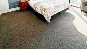 A hotel room with a large bed, two bedside tables, a window with curtains, and a view of the outdoors. - April Three Bedroom Apartment (Lake Tekapo)