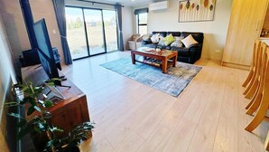 A spacious living room with a large window, a sofa set, a coffee table, and a TV. - April Three Bedroom Apartment (Lake Tekapo)
