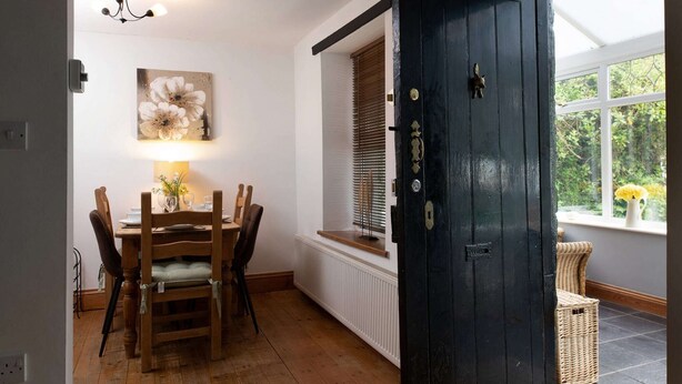A dining area with a wooden table and chairs, a wall-mounted lamp, and a black door with a window above it.