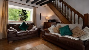 A cozy living room with two brown leather sofas, a wooden staircase, and a large window with curtains.