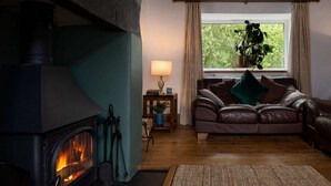 A cozy living room with a fireplace, a leather sofa, a window with curtains, and a lamp on a side table.