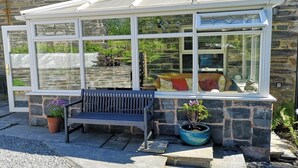 A conservatory with a bench and potted plants, set against a stone wall.