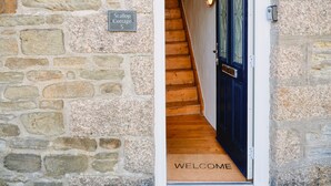 A stone wall with a sign reading "Scallop Cottage 5" and a wooden staircase leading to a dark blue door with a "WELCOME" mat. - Cottage in Porthleven near St Michael’s Mount (Porthleven)