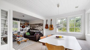 A spacious room with a white ceiling, a dining table with chairs, a bookshelf, a sofa, and a large window with a view of greenery. - Ref. 534251 (Saltsjö-Boo)
