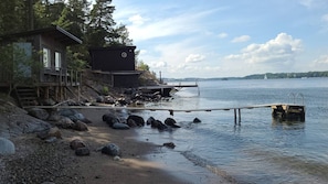 A wooden cabin with a deck, a dock extending into calm water, and a rocky shoreline.