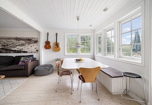 A room with a dining table, chairs, a sofa, a bean bag, and guitars on the wall.