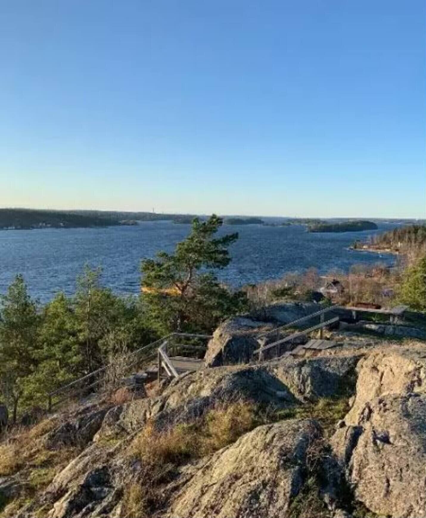 Eine Küstenlandschaft mit felsigem Gelände, einem hölzernen Steg und Blick auf das Meer und das entfernte Land.