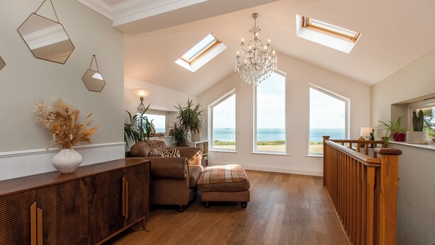 A spacious living room with a wooden floor, a large chandelier, and a view of the ocean through large windows.