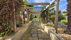 A pathway leading through a garden with a wooden pergola overhead.