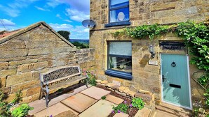 A stone cottage with a green door, a bench, and a satellite dish. - Cottage in Glaisdale by North Yorkshire Moors (Whitby)
