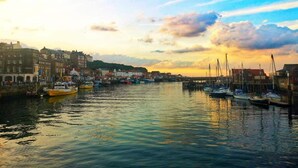 A harbor with boats docked, buildings along the waterfront, and a sunset in the background. - Cottage in Glaisdale by North Yorkshire Moors (Whitby)