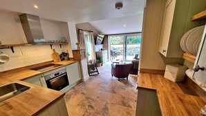 A modern kitchen with a stone tile floor, wooden countertops, and a dining area with a purple chair and a table. - Cottage in Glaisdale by North Yorkshire Moors (Whitby)