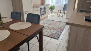 Eine moderne Küche mit einer Holzarbeitsplatte, einem eingebauten Backofen und einem Spülbecken. Es gibt einen Essbereich mit einem Holztisch und Stühlen, sowie einen farbenfrohen Teppich auf dem Boden.