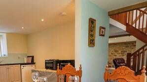 Comedor con una mesa dispuesta para cuatro, cocina al fondo y una escalera que sube a un nivel superior.