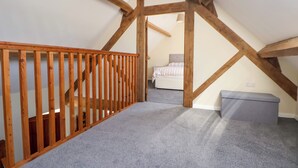 Una habitación con techo inclinado, vigas de madera, una escalera, una cama y un banco.