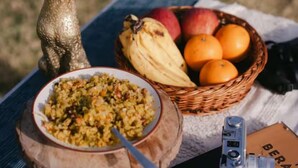 A table with a bowl of food, a basket of fruit, a camera, and a book. -  Jaadooghar Aravalli Hideaway Jawai (Bali)