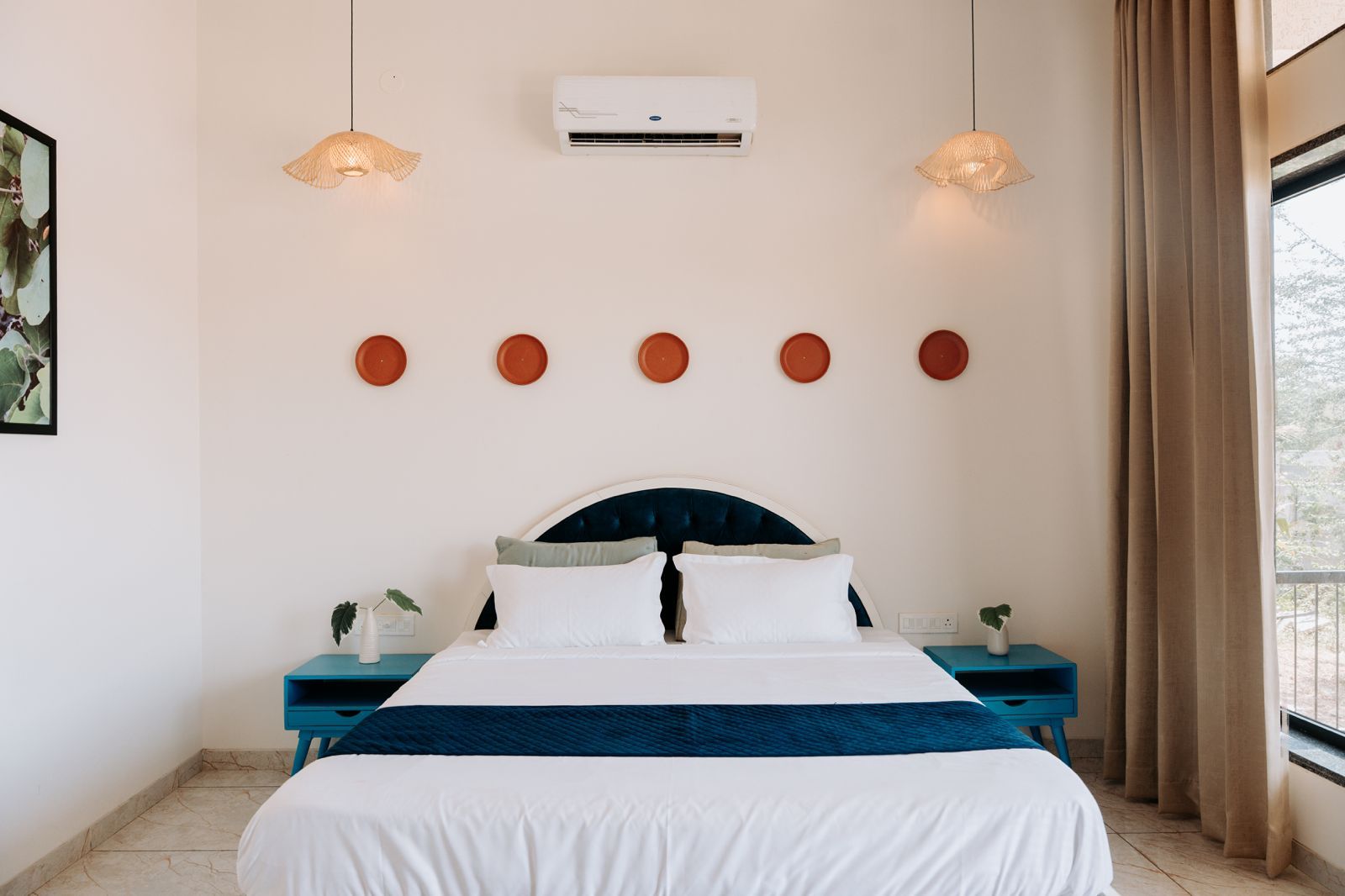 Ein Hotelzimmer mit einem Bett, zwei Nachttischen, einer Wand-Klimaanlage und einem Fenster mit Vorhängen.