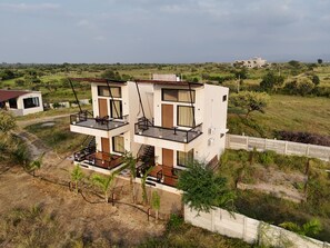 Ένα σύγχρονο διώροφο σπίτι με μπαλκόνι, που περιβάλλεται από ένα καταπράσινο τοπίο και λίγα δέντρα.