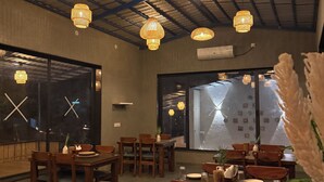A restaurant interior with wooden tables and chairs, hanging wicker lamps, and large windows with views. - Jawai Retreat - Jawai (Bali)