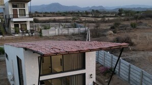 A modern two-story house with a flat roof, large windows, and a fenced backyard. -  Jaadooghar Aravalli Hideaway Jawai (Bali)
