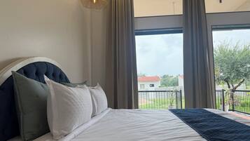 A bedroom with a large bed, a headboard, and a view of a balcony with a railing.