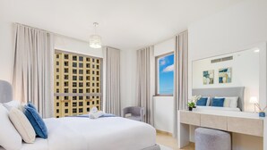 A modern hotel room with a large bed, a desk with a mirror, and a view of a building through the window.