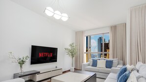 A modern living room with a flat-screen TV displaying "NETFLIX," a sofa, a coffee table, and a large window with a city view.