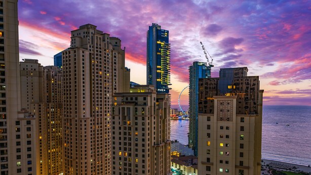 A high-rise hotel with multiple floors, a view of the sea, and a colorful sunset sky.