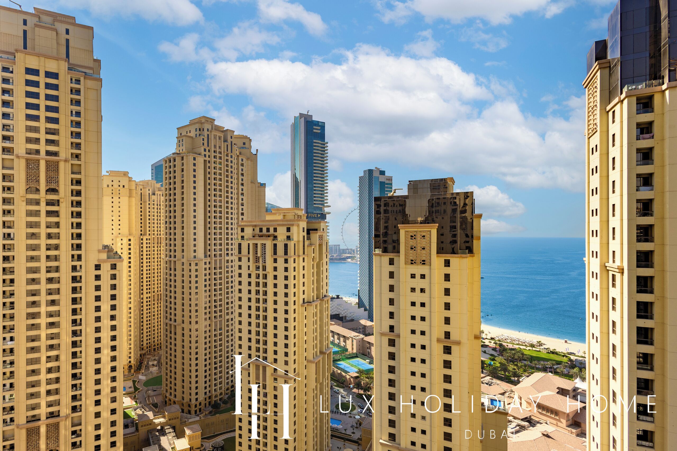 A high-rise building complex with multiple residential towers, a view of the beach, and the Dubai Marina in the background.