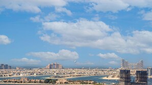 A coastal cityscape with a prominent hotel featuring a large archway, surrounded by modern high-rise buildings and a clear blue sky.
