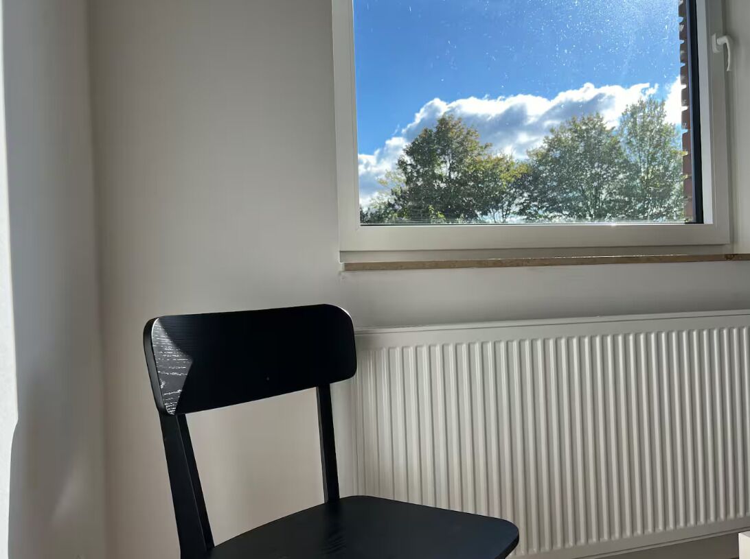 A room with a window, a radiator, and a black chair.