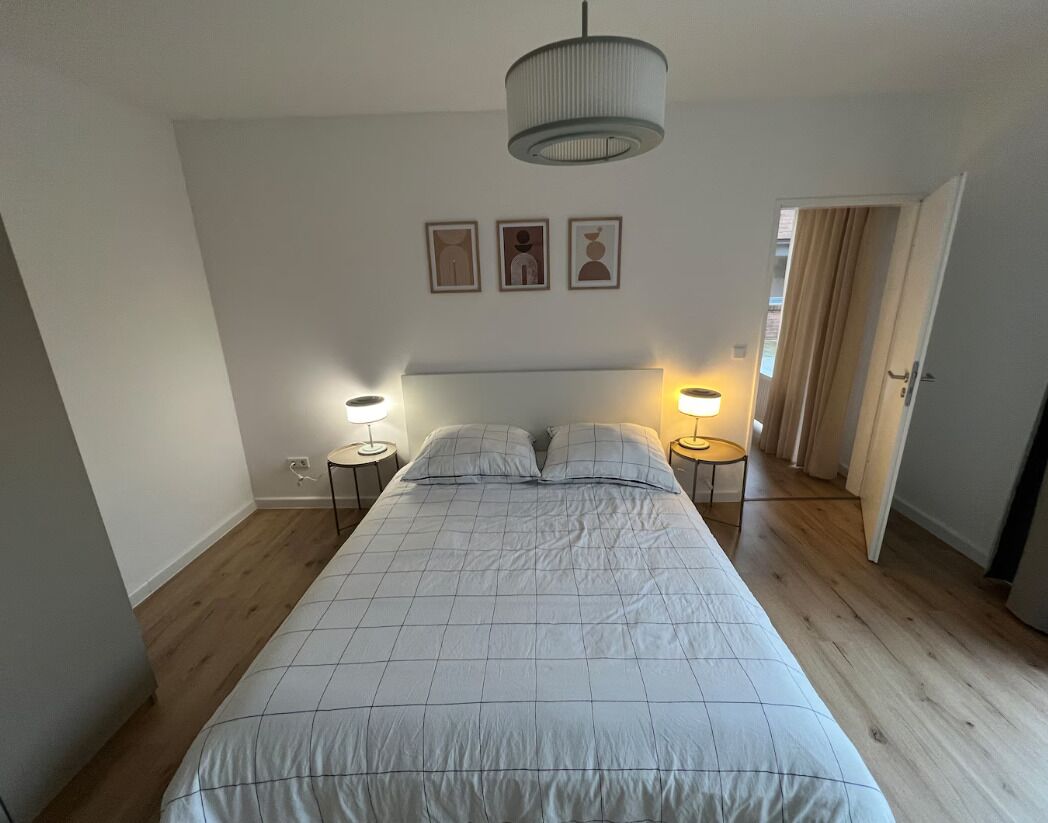 Un dormitorio con una cama grande, dos mesitas de noche con lámparas, una luz de techo y tres cuadros en la pared.