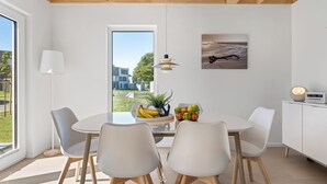 A modern dining area with a round table, white chairs, a fruit bowl, and a view of the outdoors. - Haus Fabelhaft - Terrace, 2 Bathrooms, Fireplace, Infrared Sauna, SodaStream (Olpenitz)