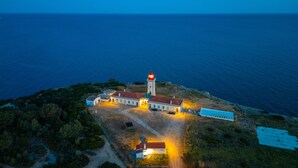 An aerial view of a coastal building complex with a lighthouse, surrounded by vegetation and a clear view of the sea. - Villa Farol Boutique (Lagoa)