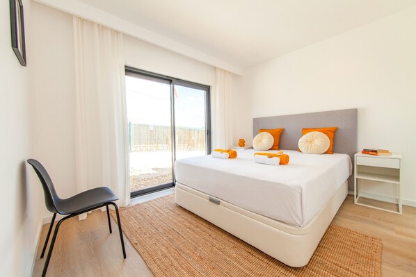 A modern hotel room with a large bed, a chair, a nightstand, and a view through a sliding door. - Villa Farol Boutique (Lagoa)