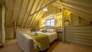 Une chambre avec un plafond en pente, un lit recouvert d’une couverture verte et deux lampes de chevet.
