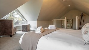 Un dormitorio amplio con una cama grande, una ventana, una silla y una escalera.
