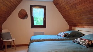 A bedroom with two beds, a window, a chair, and wooden paneling on the walls.