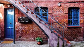 A brick building with a blue door, a metal staircase, and a potted plant.