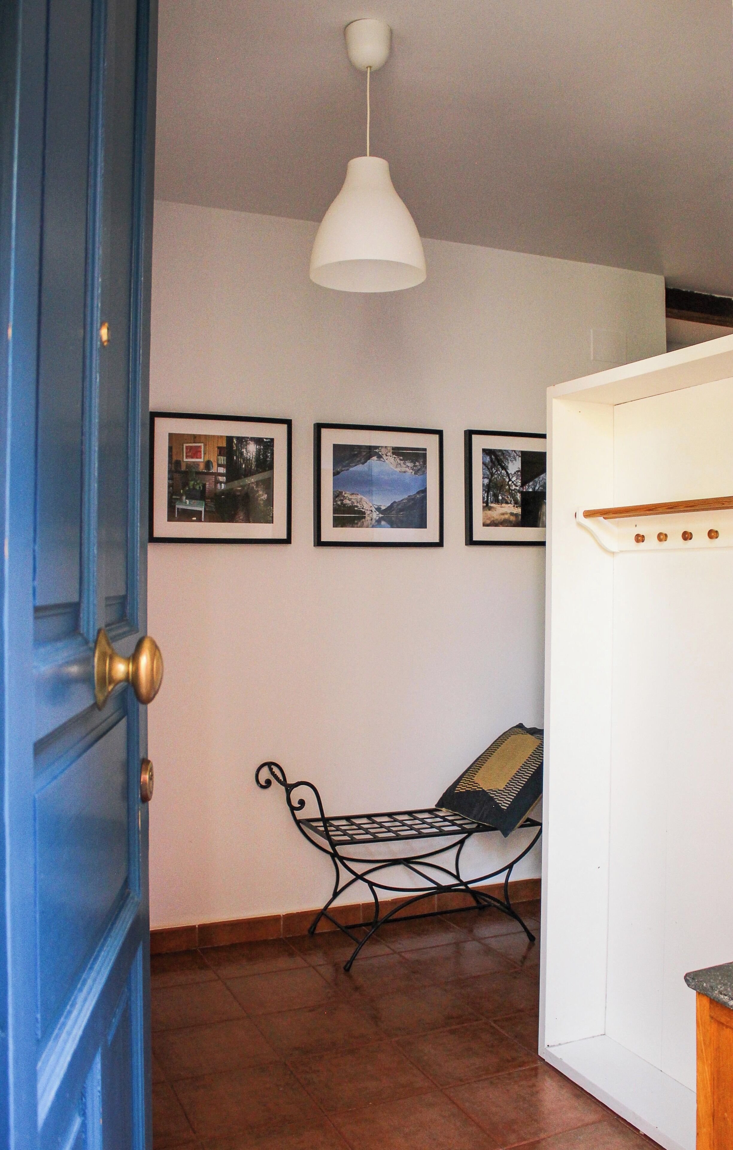 A room with a blue door, a white wall with framed pictures, a black metal bench, and a white ceiling light.