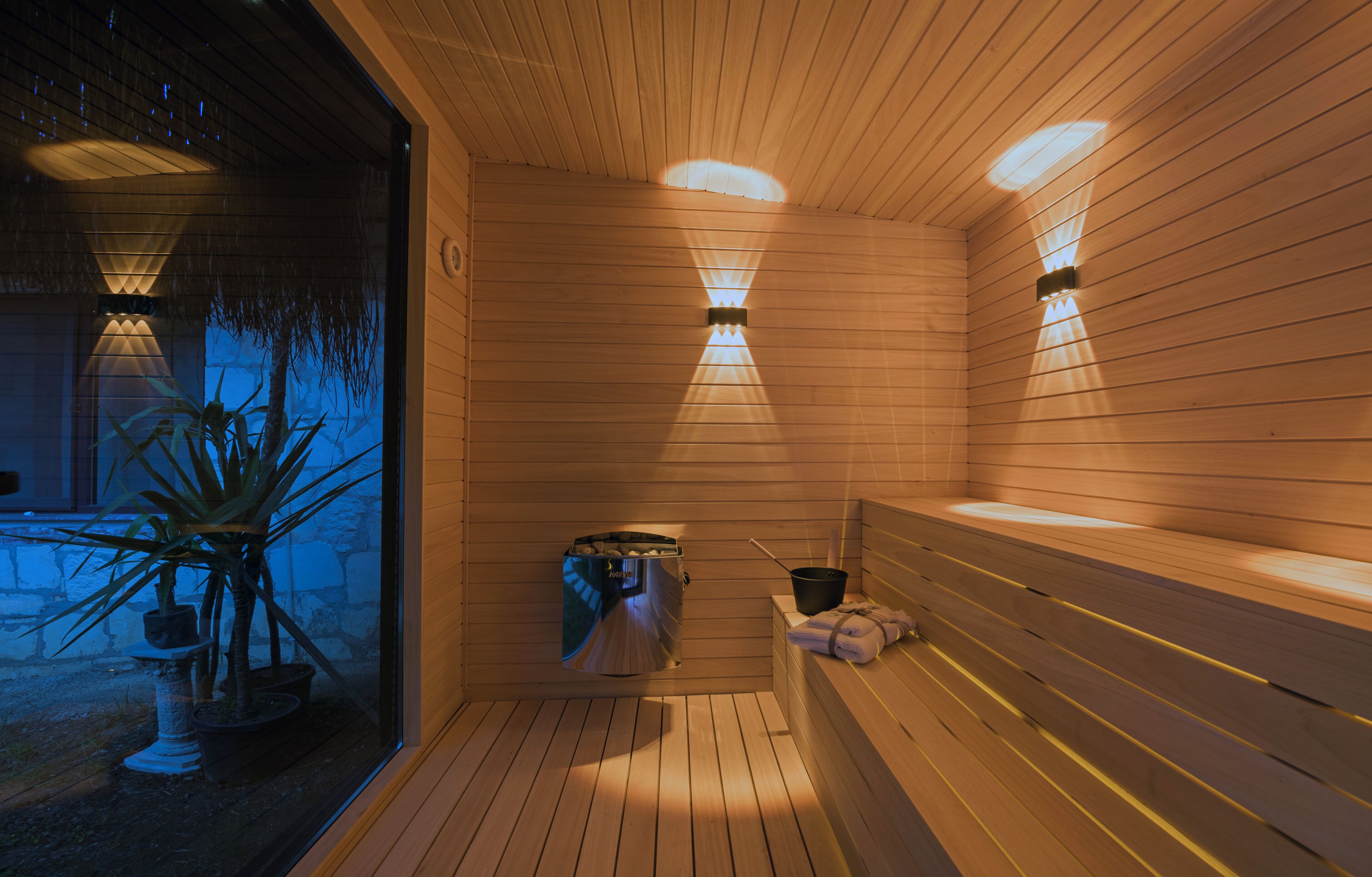 Una sauna con paredes y bancos de madera, un calentador y una ventana con plantas en macetas.