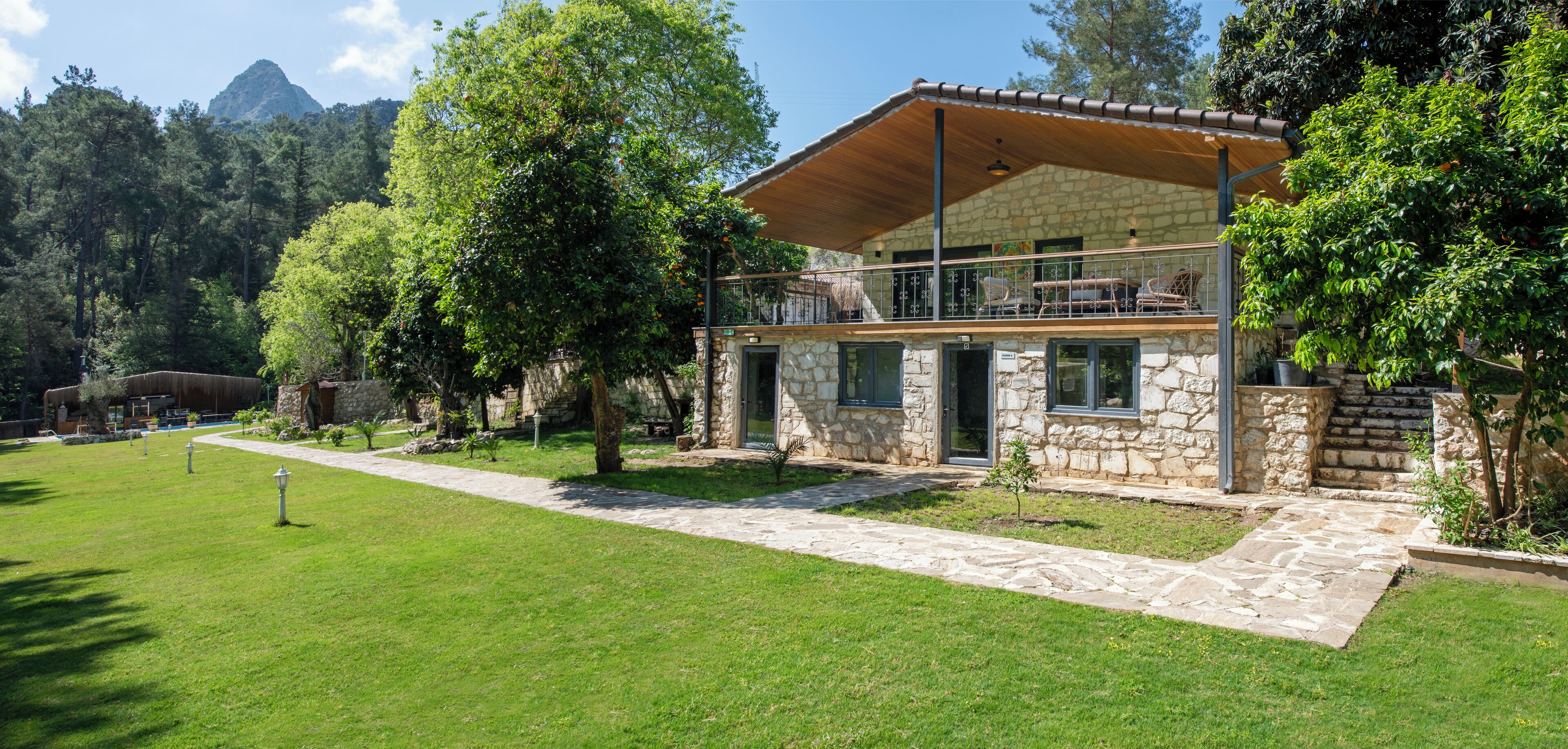 A stone building with a balcony, surrounded by lush greenery and a stone pathway.