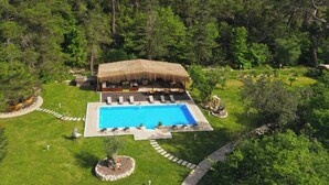 A resort with a pool, lounge chairs, and a thatched-roof building surrounded by dense forest and mountains. - YUSALİS GARDEN HOTEL (Kumluca)